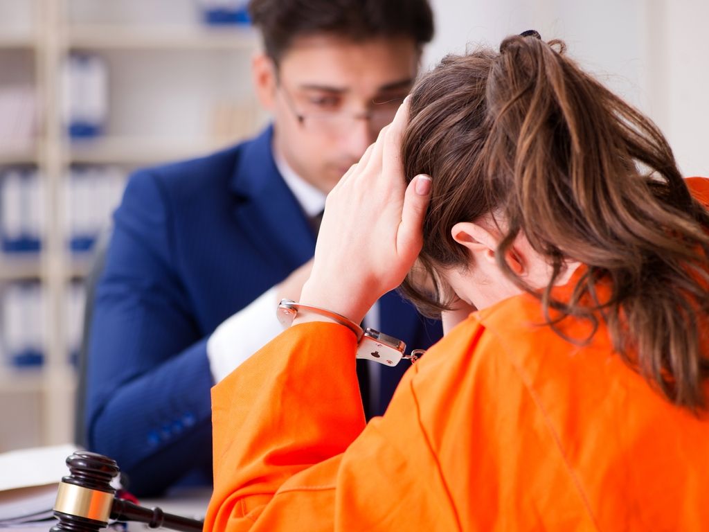 woman prisoner in cuffs holding head in hands in front of lawyer
