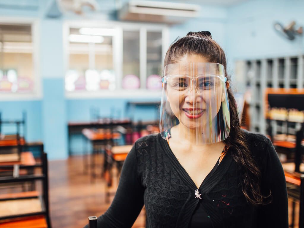 female teacher standing in classroom with face shield on